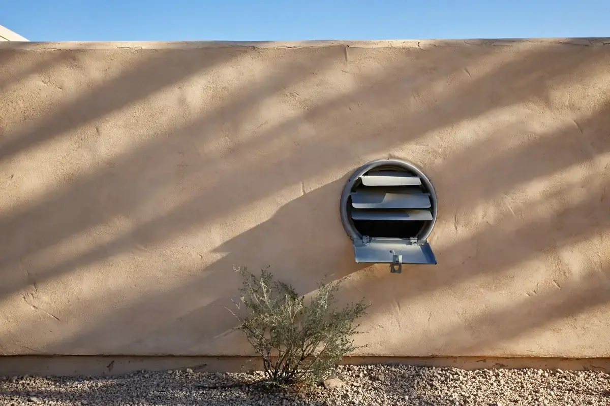 Stucco wall outside a home with a louvered dryer vent cap and gravel landscaping