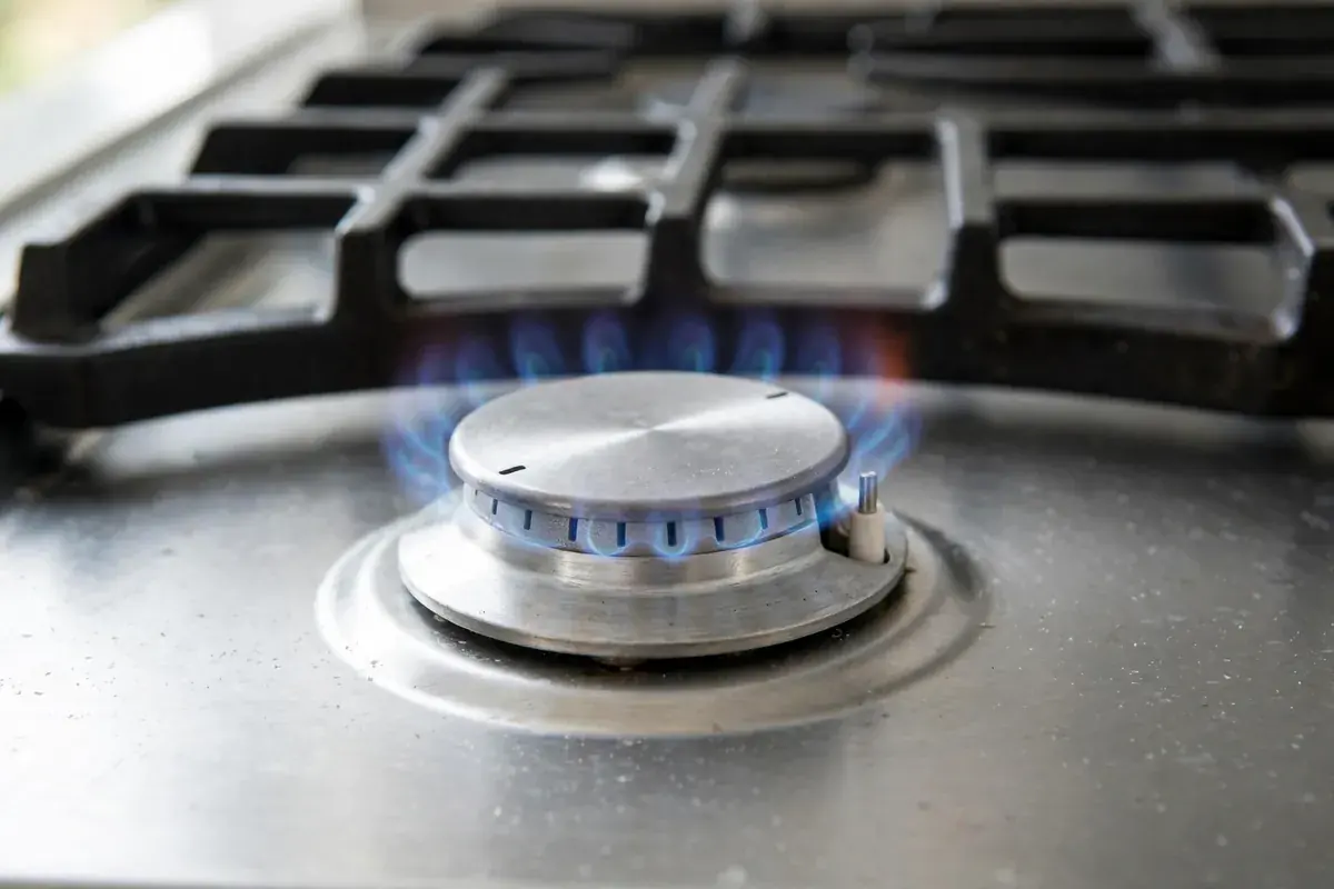 Gas range burner with a small steady blue flame at the igniter